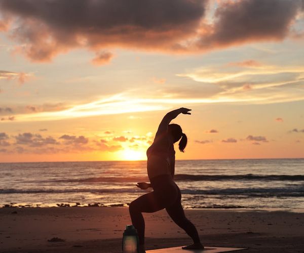 Person stretching on a yoga mat during sunrise.